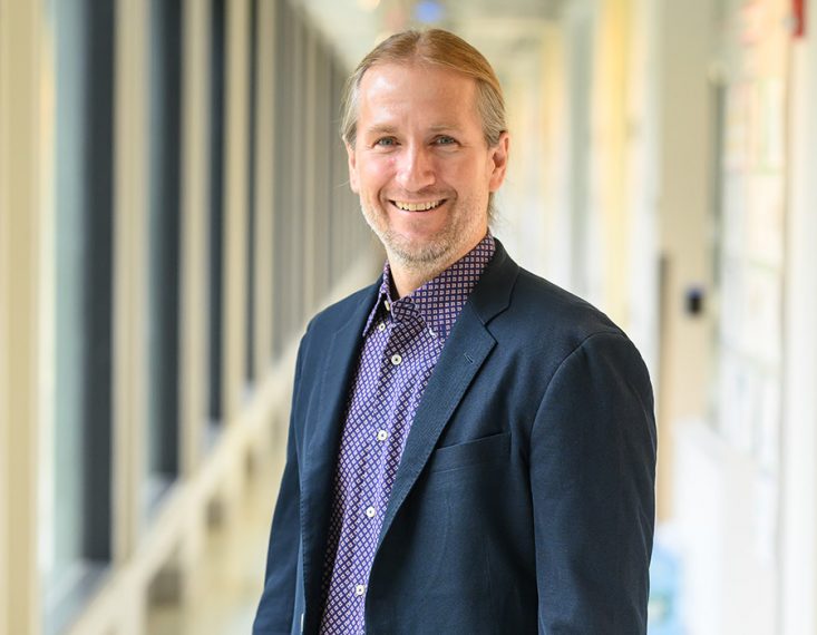 Professor Jeremiah Johnson smiles in a hallway.