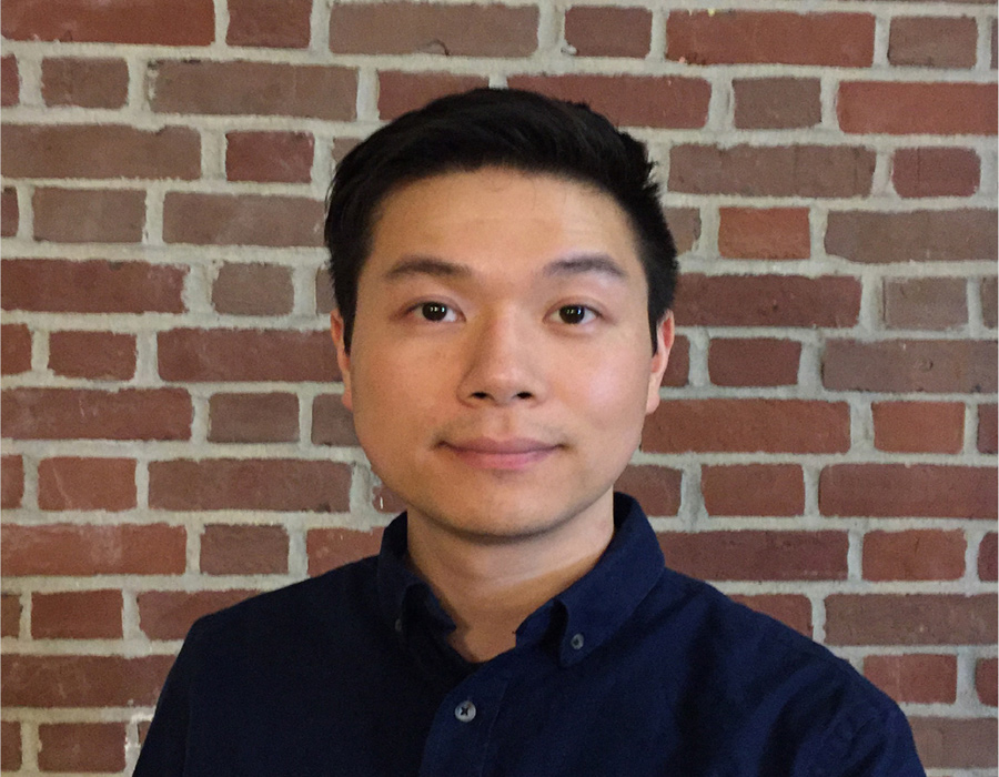 Graduate Student Kenny Chen stands before a brick wall