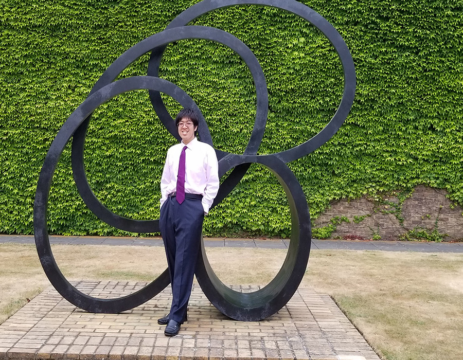 Graduate Student Henry Tran poses outdoors in front of a sculpture.