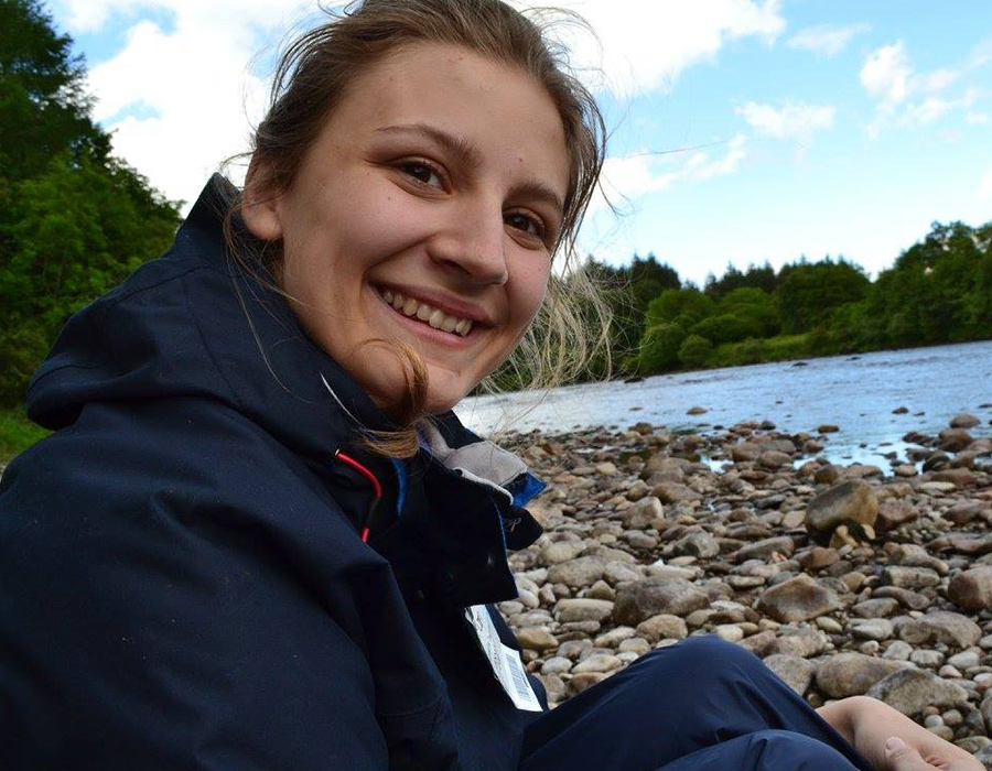 Chemistry Major Ruth Tweedy sits on a pebbly beach.