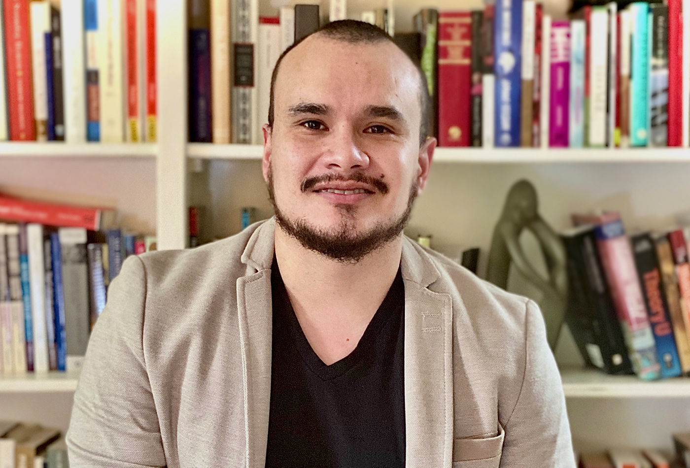 A man sits in front of a bookshelf.