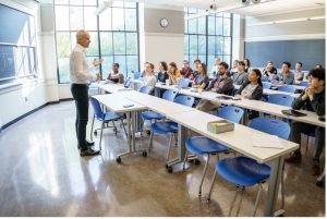 Moungi Bawendi stands at the front of a classroom facing several rows of MIT students.