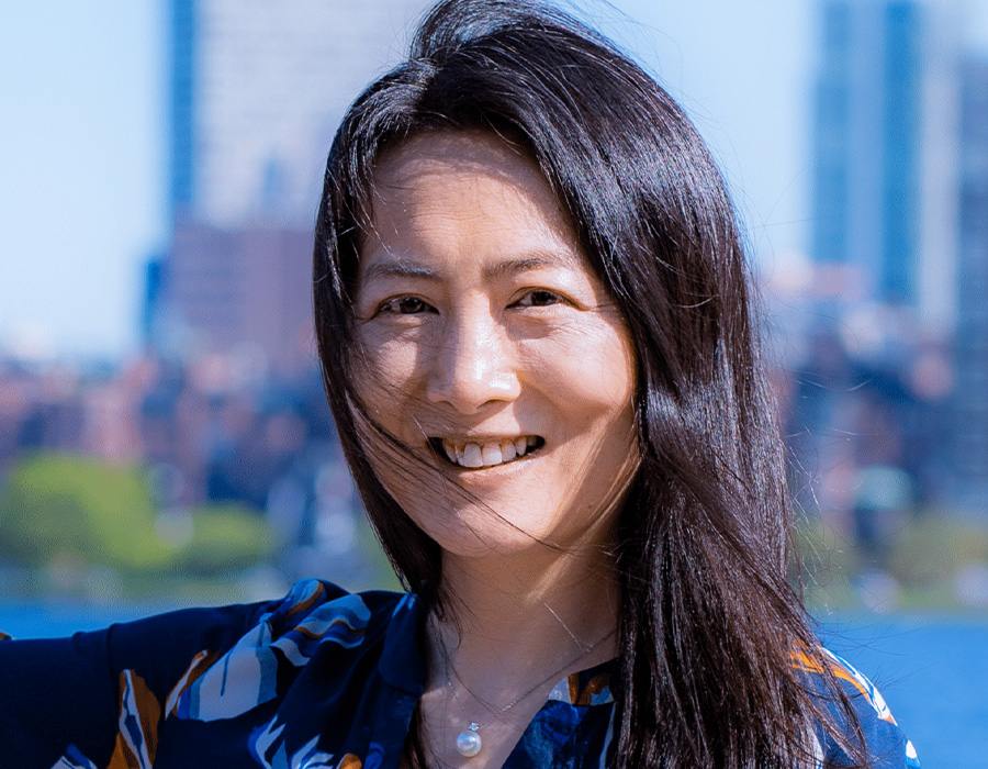 Yang Shao-Horn smiles outdoors with the Boston skyline behind her.